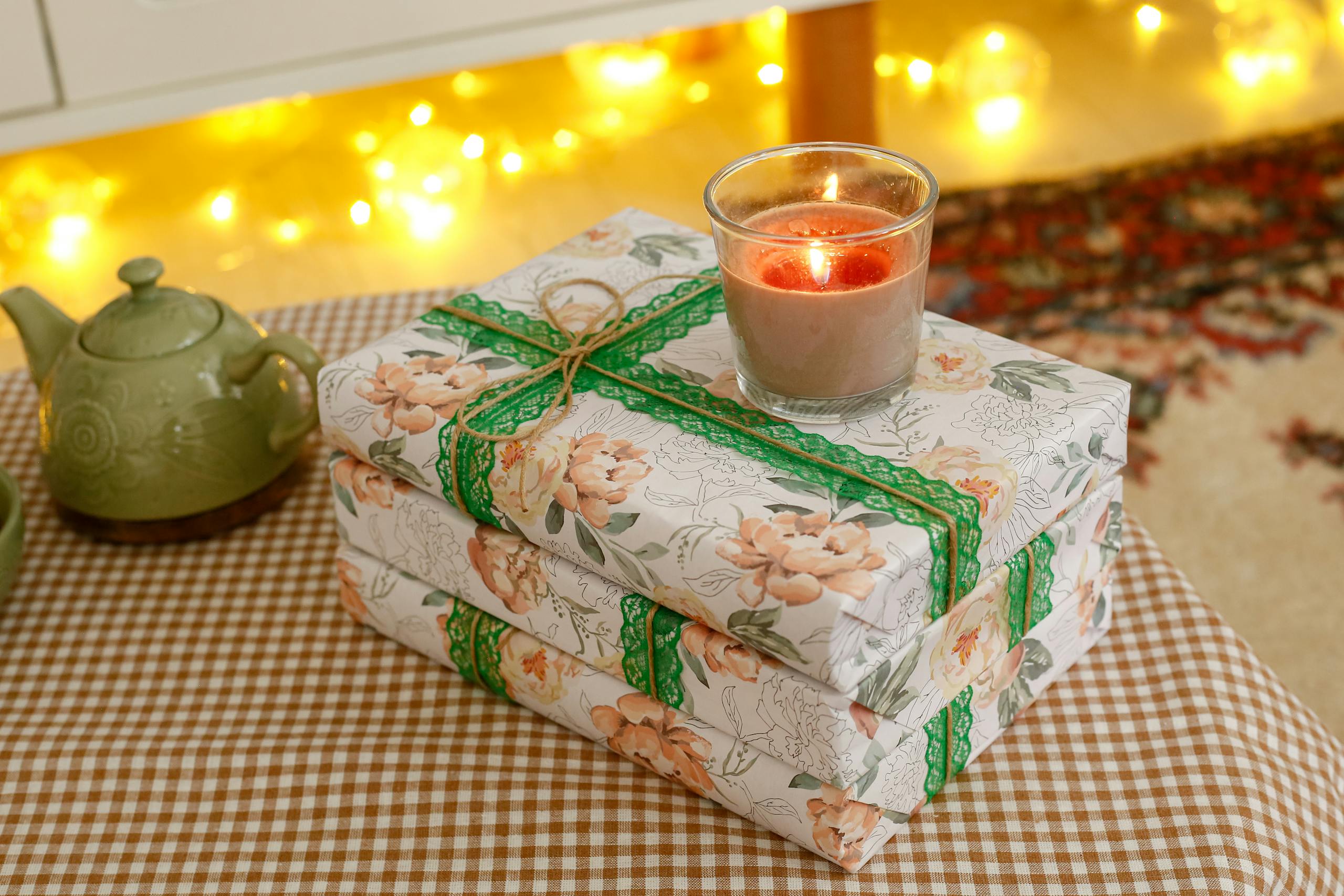 Floral-wrapped holiday gift with candle on checkered tablecloth, perfect cozy holiday setting.
